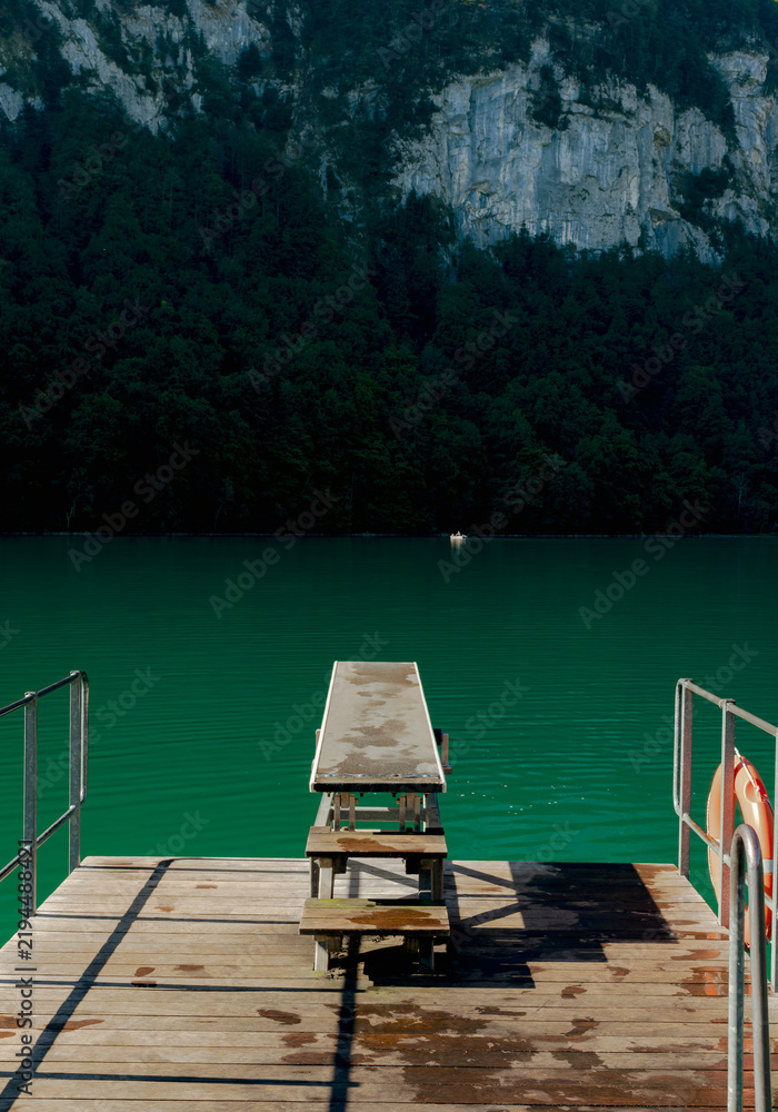 Fototapeta premium Diving board and life buoy on a dock over a green alpine lake