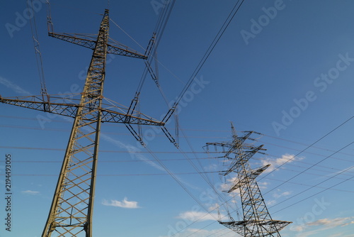 Low-angle view of a steel electricity transmission tower with multiple high voltage power lines and insulators crossing a clear blue sky