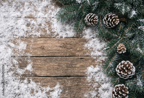 Rustic wooden board surrounded by pine cones and evergreen branches in snowy winter setting