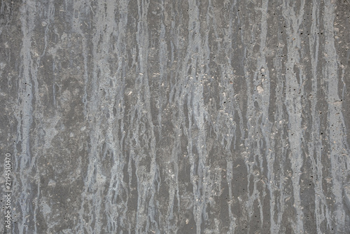 Close-up of a gray concrete wall with vertical water stains, streaks, pores and rough surface details.