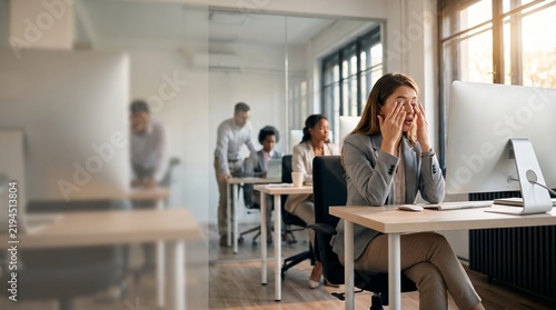 Stressed businesswoman rubbing eyes at office desk, tired female employee suffering from eye strain, exhausted professional worker in modern workspace