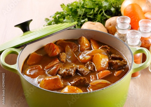 Quadro su tela Beef stew in a green dutch oven with fresh vegetables on a wooden table