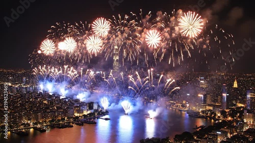 Spectacular fireworks display over New York City at night, with red and gold bursts illuminating the skyline above the East River, Empire State Building, and illuminated skyscrapers.