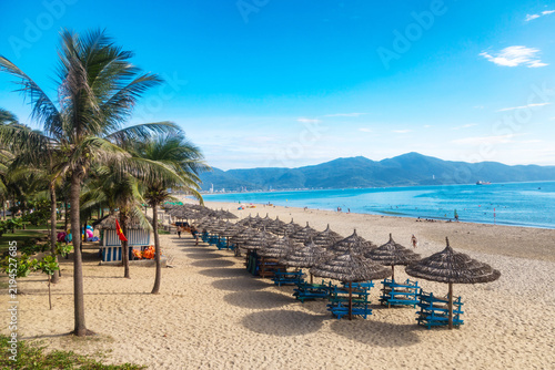 My Khe beach in Da Nang with palm trees, thatched umbrellas, sun loungers, turquoise sea, and mountains in the background