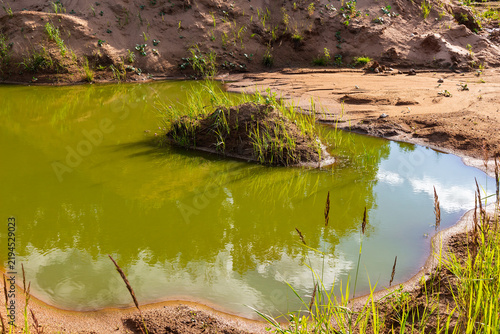 Konstfotografi Green stagnant water pooling inside an old sandy quarry, with a small grassy isl