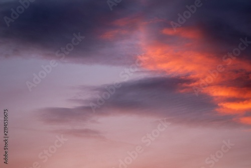Dark gray clouds contrast with brilliant orange and pink sunset light, forming a powerful cloudscape ideal for weather, nature, atmospheric, and background concepts.