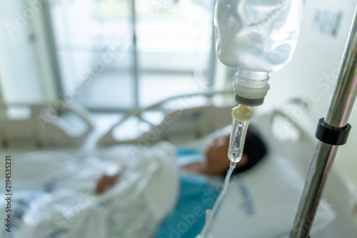 Obraz na plátne A close-up of a saline bottle strapped to a needle pricked at the hand of a female patient lying in a hospital bed