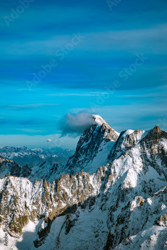 View of the snow-capped Mont Blanc peak under a clear blue sky with a small cloud clinging to the summit in Chamonix, Auvergne-Rhone-Alpes, France.