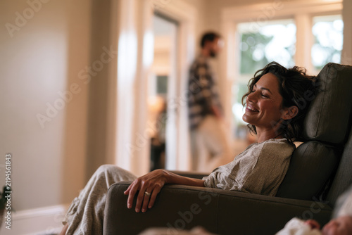 A smiling woman enjoying a relaxing moment in an armchair, signifying happiness and contentment in a stylish living space filled with natural light.