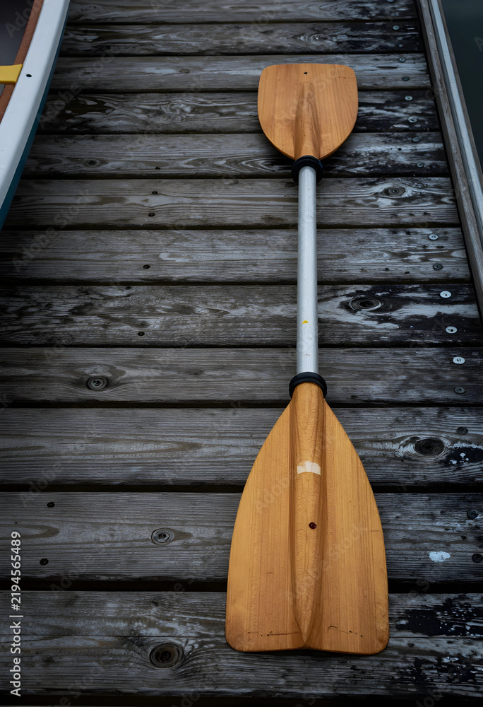 Fototapeta premium Outdoor recreation and adventure travel, wooden kayak paddle resting on a weathered wooden dock by the water for summer vacation and leisure activity