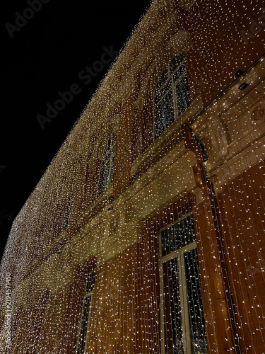 Brick building facade is decorated with vertical hanging strands of warm white fairy lights at night