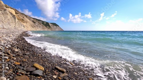 Pebble beach with sea waves breaking on shore near cliffs, scenic coastal landscape, summer vacation destination.