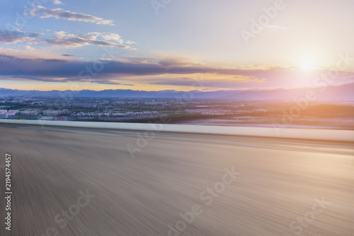 A wide flat open ground overlooks a distant city and mountain range under a colorful sunrise sky.