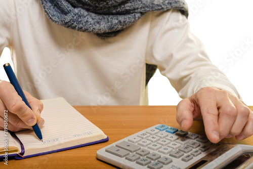 Closeup photo of man planning budget with calculator while writing notes in notebook Recording expenses for better money management and budget control