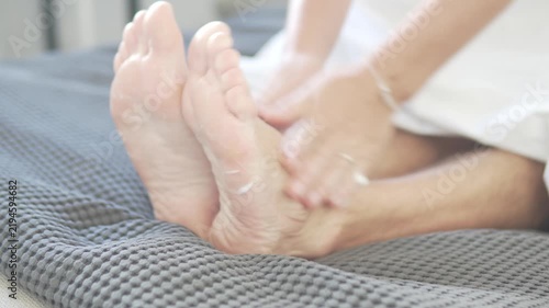 Close-up of a person applying moisturizing cream to bare feet while relaxing at home. Foot care, skincare and self-care routine with lotion on dry skin