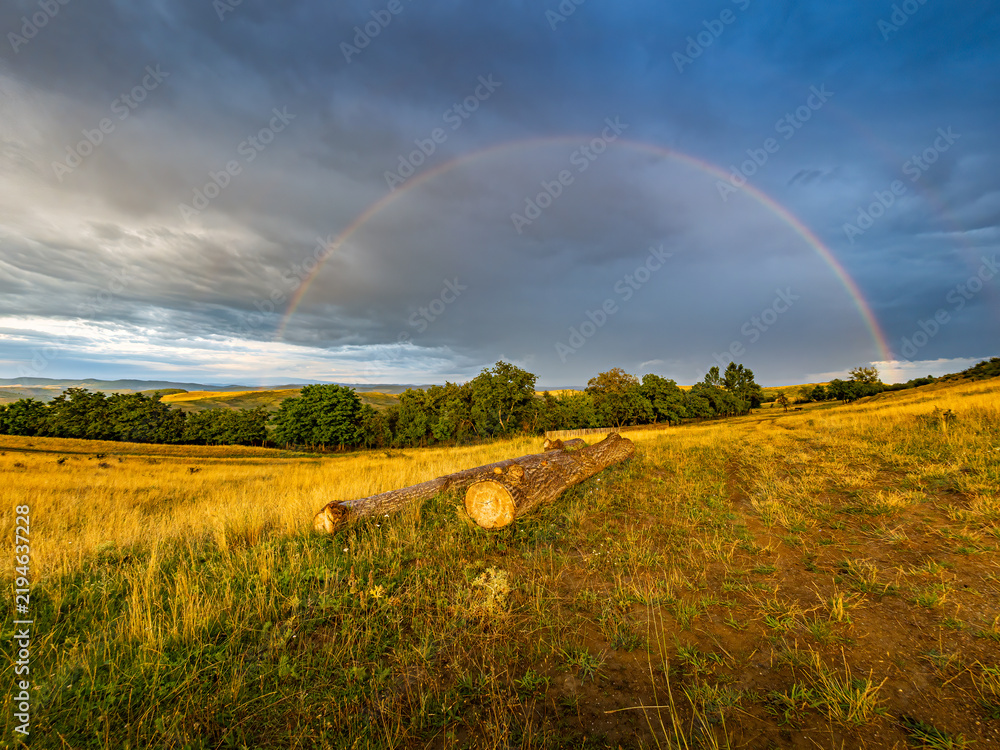 Obraz premium Faint Rainbow Beneath Dramatic Storm Clouds After Rain at Sunrise