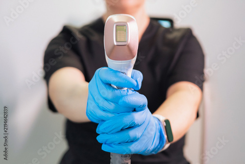 Bild auf Leinwand Beautician holding laser hair removal machine handpiece in blue gloves