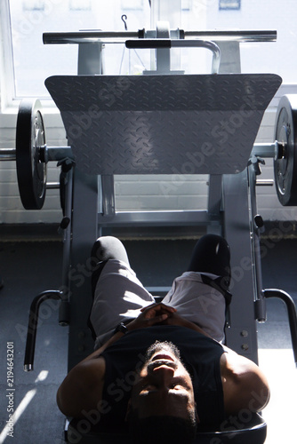 Foto African male lying on leg press machine at gym, wearing fitness tracker, showing