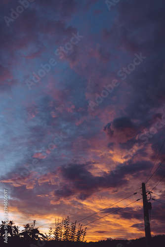 Vibrant sunset sky painted with dramatic purple and orange clouds over a silhouetted rural landscape.