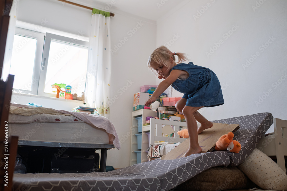 Fototapeta premium little girl balancing and jumping on mattress slide during active play at home