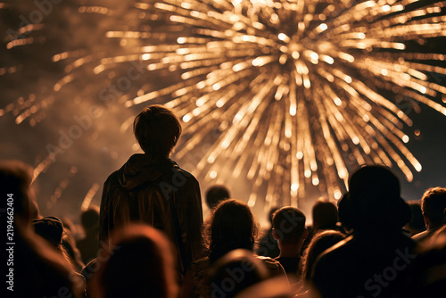Back view of people watching golden fireworks display at night