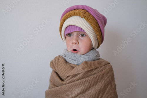 surprised little girl wearing multiple warm winter knitted beanies