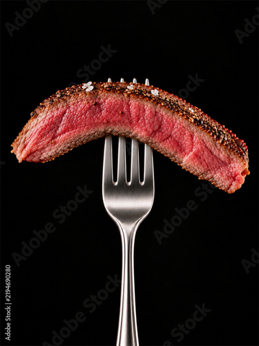 Medium Rare Pepper Crusted Beef Steak Slice on Fork Isolated on Black Background.