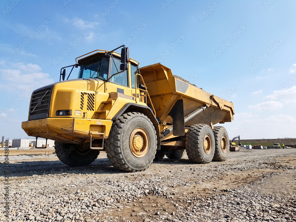 Fototapeta premium Large yellow dump truck parked on gravel construction site under