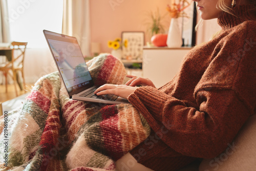 Woman using laptop under blanket at home.