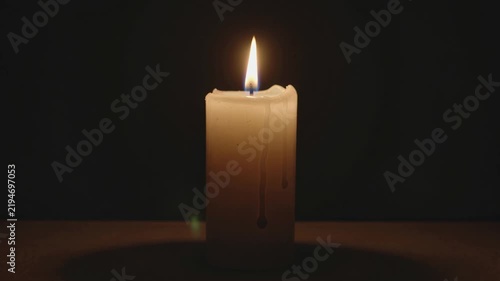Cinematic video of a single white candle burning with a steady warm flame and melted wax against a deep dark background.