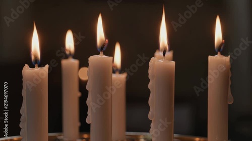 Cinematic video of several white candles burning with warm flickering flames and melted wax against a dark softly blurred background.