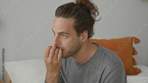 Картината върху платно Man bites fingernails with hand to mouth on bed in bedroom, seated and slightly tense; anxiety introspection