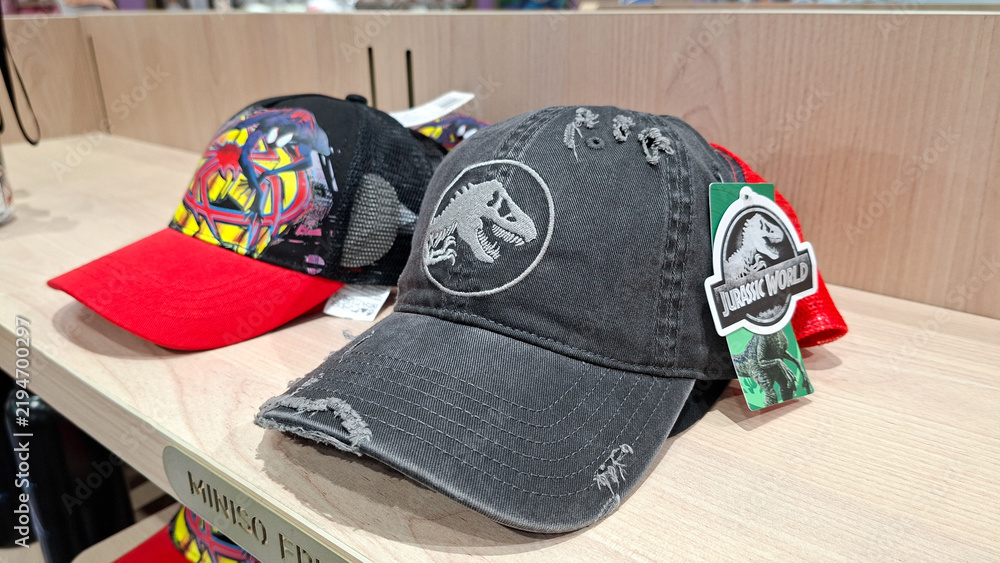 Fototapeta premium jurassic world washed grey distressed baseball cap with embroidered t rex logo on wooden retail shelf next to spider man hat on September 16, 2026 in Bangkok, Thailand.
