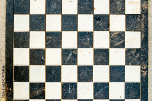 Fotografie A worn chessboard surface with black and white squares, closeup of chess table at the park