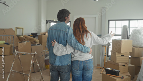 Konstfotografi Man embraces woman with arm around waist among stacked moving boxes in a building; hopeful new start