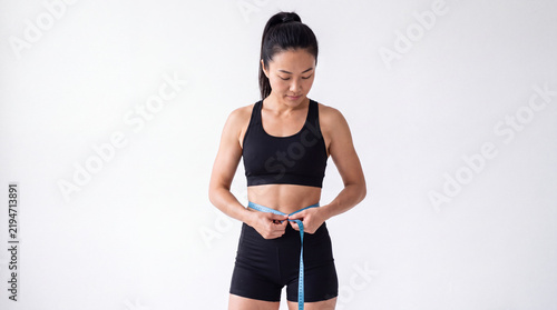 Athletic Young Woman Measuring Her Waist with a Tape Measure against White Background