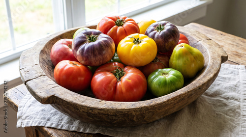Assorted heirloom tomatoes in a rustic wooden bowl on a wooden table