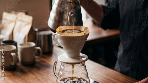 Barista pouring hot water over coffee grounds in a white ceramic dripper for pour over coffee