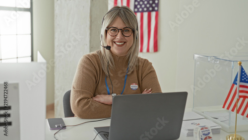 Foto Woman wearing headset and glasses types on laptop at polling station table with clear ballot box and i voted sticker in building; civic duty friendly