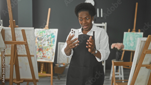 Obraz na plátně Woman painter holding smartphone and smiling, hands visible while checking phone in art studio; creative joy