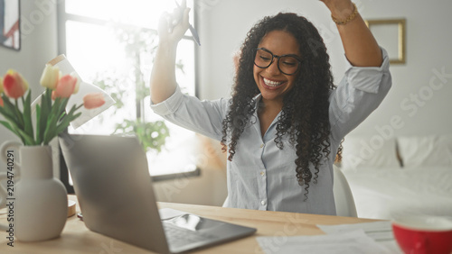 Bild auf Leinwand Woman at laptop raises arms and claps smiling in a home office studio with tulips and papers on desk; work success celebration