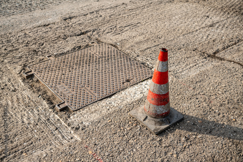 Traffic cone and square manhole cover on milled asphalt during road works, pavement resurfacing and street maintenance for traffic safety in urban construction site under repair