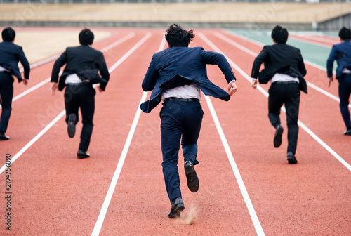 陸上トラックを全力疾走するスーツ姿のビジネスマンたち、競争社会と挑戦のイメージ