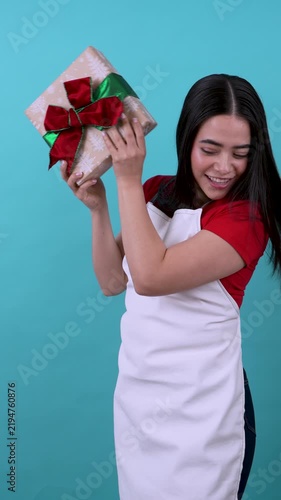 Joyful hispanic saleswoman shaking and presenting christmas gift