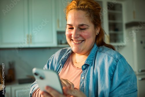 Smiling woman using smartphone in home kitchen