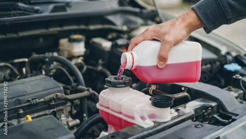 Person pouring pink coolant into a car engine reservoir