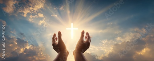 Hands raised toward a glowing cross in the sky, surrounded by radiant light and clouds, symbolizing faith and spirituality.