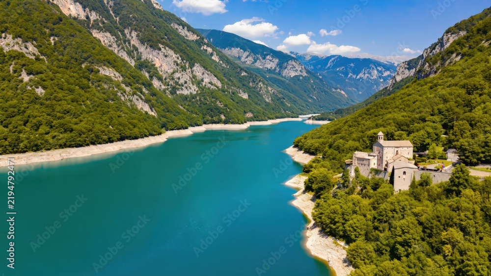 Fototapeta premium Stunning turquoise reservoir lake surrounded by lush green mountains and a historic medieval castle in the Alps, Italy.