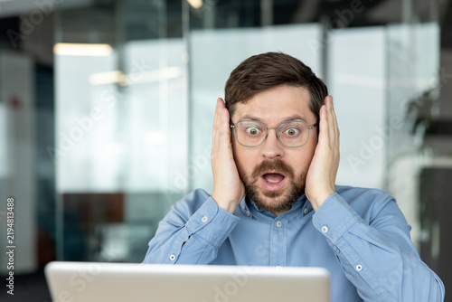 Bild auf Leinwand A frightened young man sits in an office, holding his face with his hands and lo
