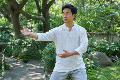 Man practicing tai chi in garden with focused expression and graceful gesture
